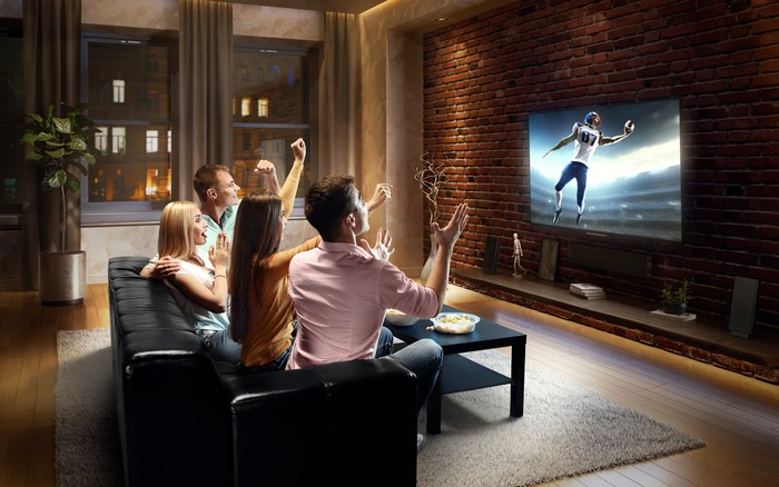 Des amis regardant un match de football à la télévision dans un salon. Ils célèbrent une prise à une main.