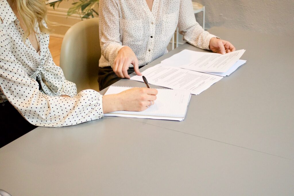 femme signant sur du papier d'imprimante blanc à côté d'une femme sur le point de toucher les documents